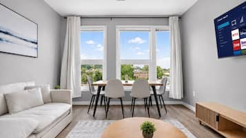 En moderne stue med sofa, spisebord, stole, sofabord og et tv der viser streamingtjenester.