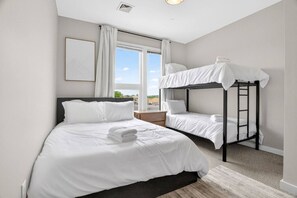 Hotellihuone, jossa on kerrossänky, yksi erillinen sänky ja suuri ikkuna, jossa on verhot.