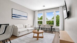 Un salon moderne avec un canapé, des fauteuils, une table basse et un téléviseur fixé au mur.