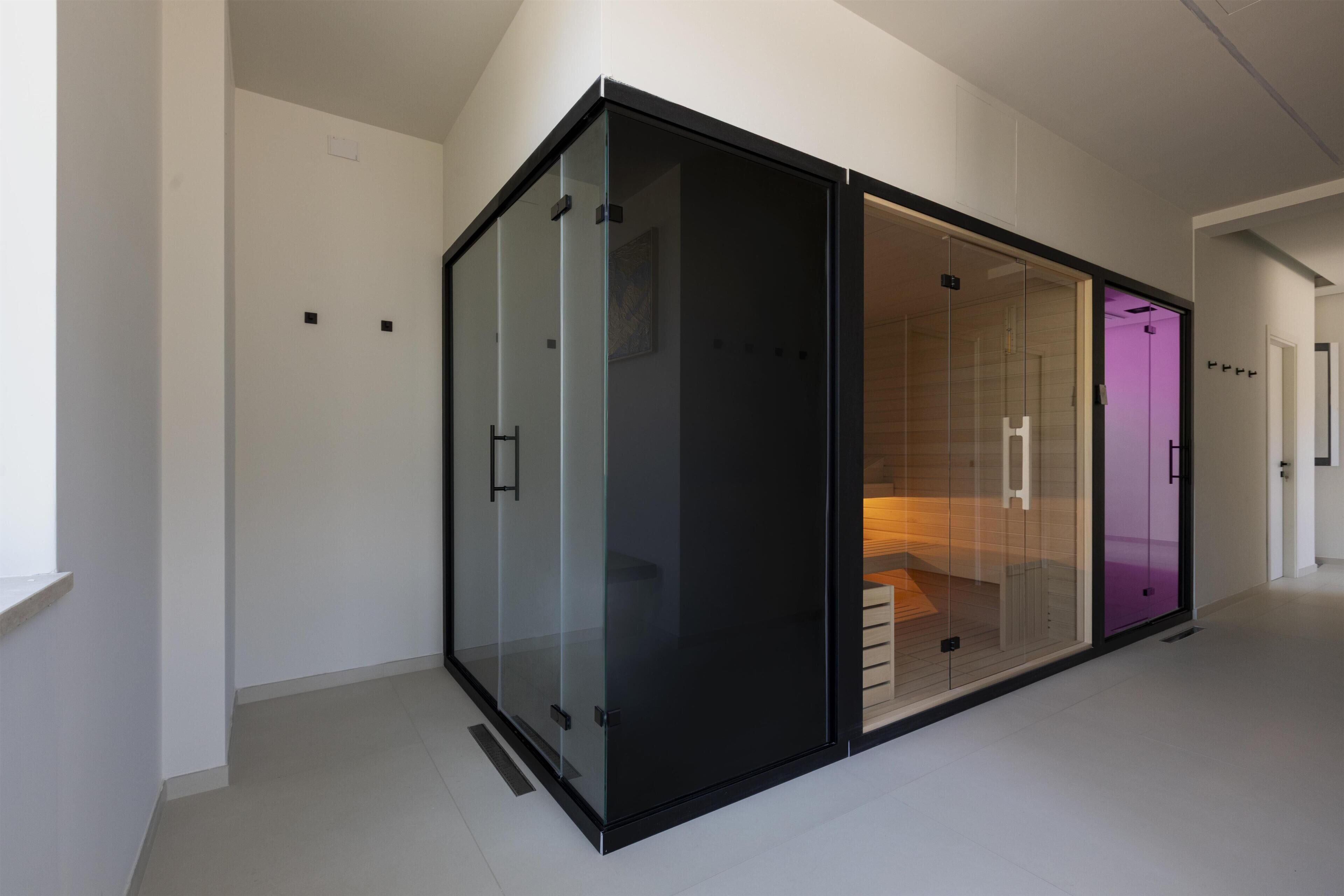 Un interior moderno con un amplio ventanal corredera de marco negro que da a una habitación con una cama y un armario iluminado en morado.