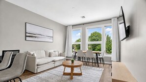 Un salon moderne avec un canapé, des fauteuils, une table basse et un téléviseur fixé au mur.