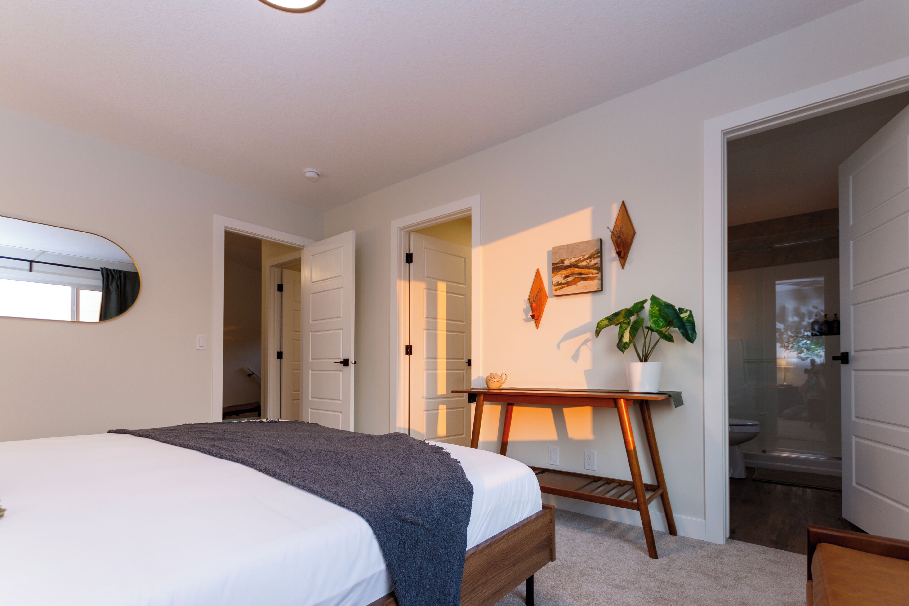 A bedroom with a bed, a bedside table, a mirror, and a potted plant.