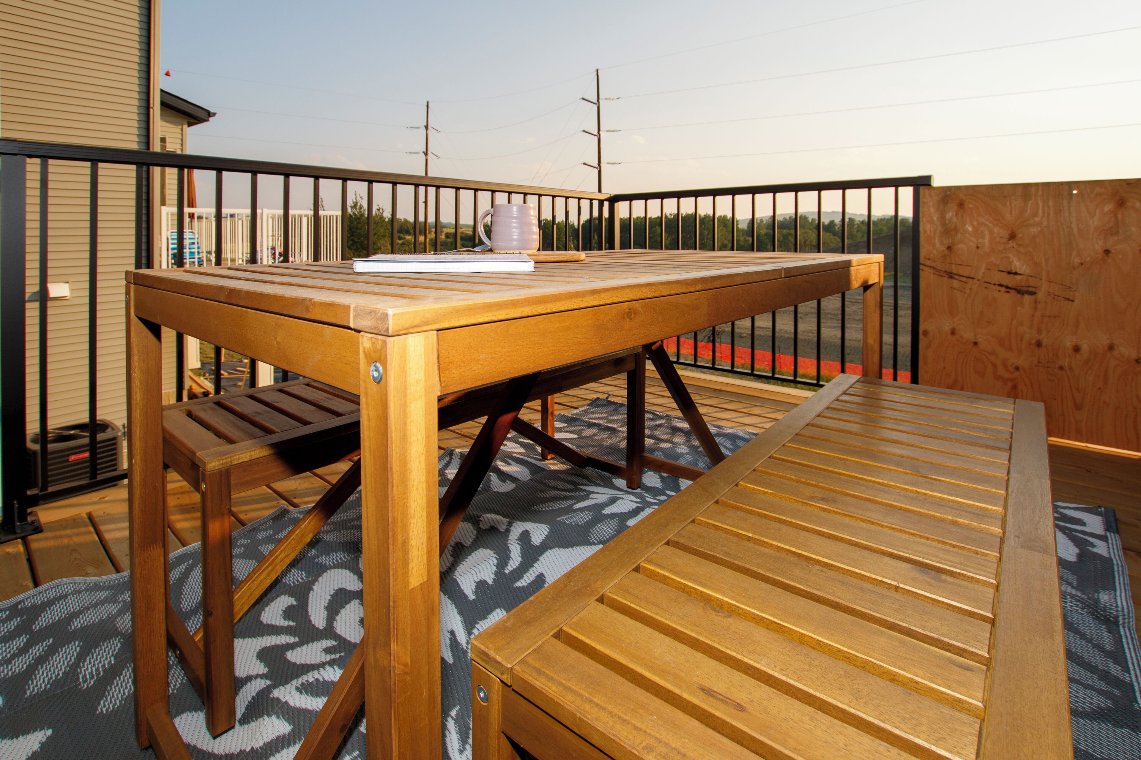 Une table en bois avec un banc, une tasse et un livre posés dessus, le tout installé sur un tapis à motifs.