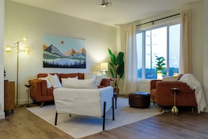 Una sala moderna con un sofá, un sillón y un cuadro de montañas.