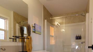 Een moderne badkamer met een witte wastafel, toilet, douchecabine van glas en een ventilatie rooster in het plafond.