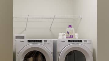 A laundry room with two Whirlpool washing machines and a shelf above them.