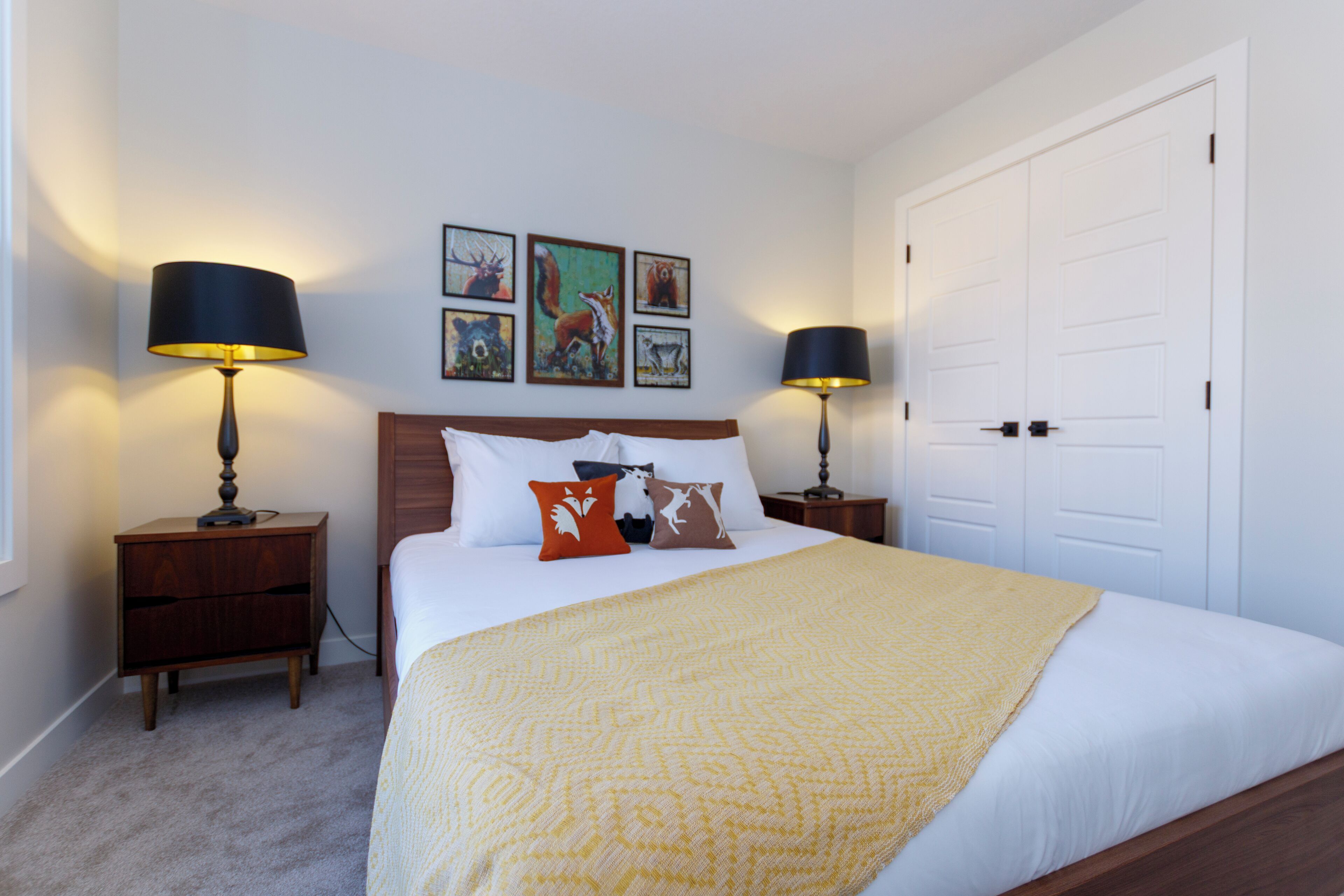A bedroom with a bed, two bedside tables, a nightstand, a door, and wall art.