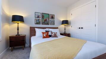 A bedroom with a bed, two bedside tables, a nightstand, a door, and wall art.