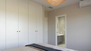 Quarto com cama, guarda-roupa e banheiro visível por uma porta aberta.