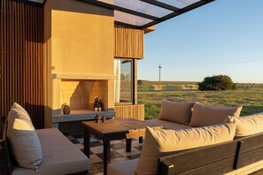 A modern outdoor seating area with a fireplace, a checkered floor, and a view of a rural landscape.