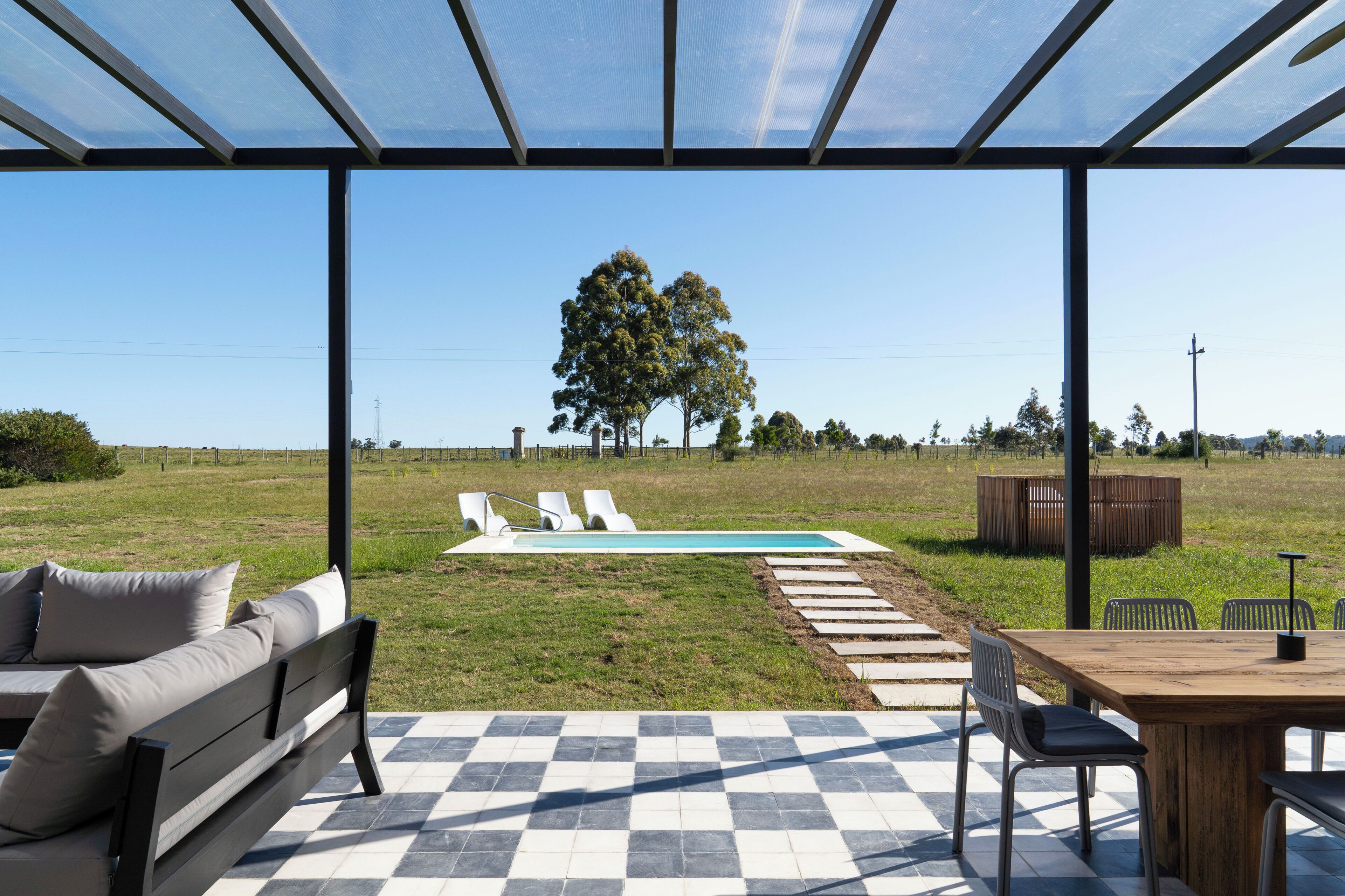 A covered outdoor area with a pool, lounge chairs, and a dining table.