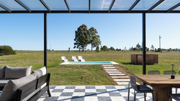 Uma área externa coberta com piscina, espreguiçadeiras e uma mesa de jantar.
