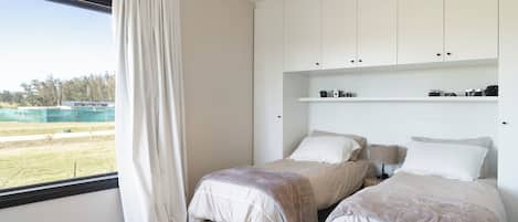 Une chambre avec deux lits, une grande fenêtre avec des rideaux, un luminaire suspendu et une étagère avec des appareils photo.