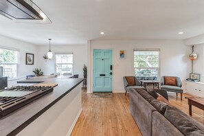 A modern kitchen with a central island, a dining area with a blue door, and a living room with a grey sofa. - West LA Beachy Bungalow (Los Angeles)