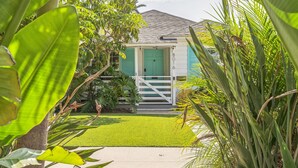 Une petite maison avec une porte verte, entourée d’une végétation luxuriante et d’une pelouse bien entretenue.