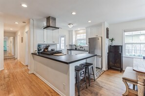 A kitchen with a central island, stainless steel appliances, white cabinetry, and a view to the outside. - West LA Beachy Bungalow (Los Angeles)