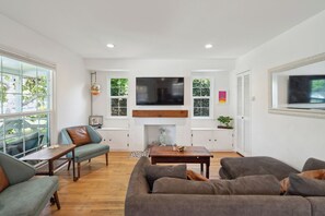 Un salon moderne doté d’une cheminée, d’un téléviseur fixé au-dessus et d’une grande fenêtre offrant une vue sur l’extérieur.