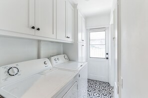 Une buanderie équipée d’un lave-linge et d’un sèche-linge à chargement frontal, de meubles blancs et d’un sol à motifs.