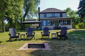 Une maison dotée d’un patio couvert, de plusieurs fauteuils Adirondack et d’un foyer extérieur.