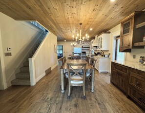 A spacious kitchen with a wooden ceiling, a dining area with a large table and chairs, and a staircase leading to another level. - Historic Lakefront Farmhouse on Battle Lake - Sleeps 9 (Battle Lake)