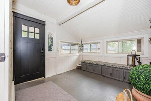 A room with a black door, a bench, a hanging light fixture, and a window with shutters. - Historic Lakefront Farmhouse on Battle Lake - Sleeps 9 (Battle Lake)
