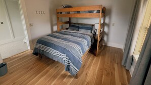 Ein Einzelzimmer mit einem hölzernen Etagenbett, einem Deckenventilator, einem Fenster mit Vorhängen und einem Holzboden.