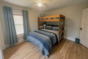 Een kamer met een stapelbed, een raam met gordijnen, een plafondventilator en een deur.