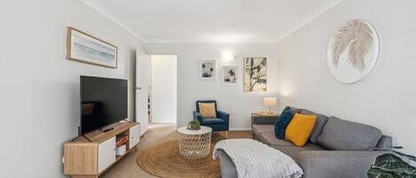 Un salon moderne avec un téléviseur à écran plat, un canapé gris, un fauteuil bleu et une table basse.