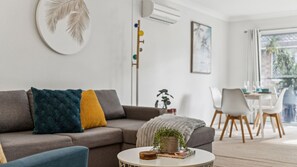 A modern living room with a sectional sofa, a round coffee table, a plant, and a dining area with chairs and a table.
