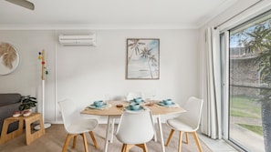 A dining area with a table set for four, white chairs, and a view of a garden through a large window.