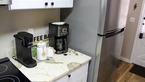 A kitchen with a coffee maker, a sugar container, and a refrigerator. - Serendipity Cottage (Prescott)