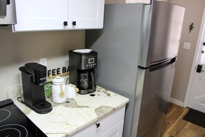 A kitchen with a coffee maker, a sugar container, and a refrigerator. - Serendipity Cottage (Prescott)