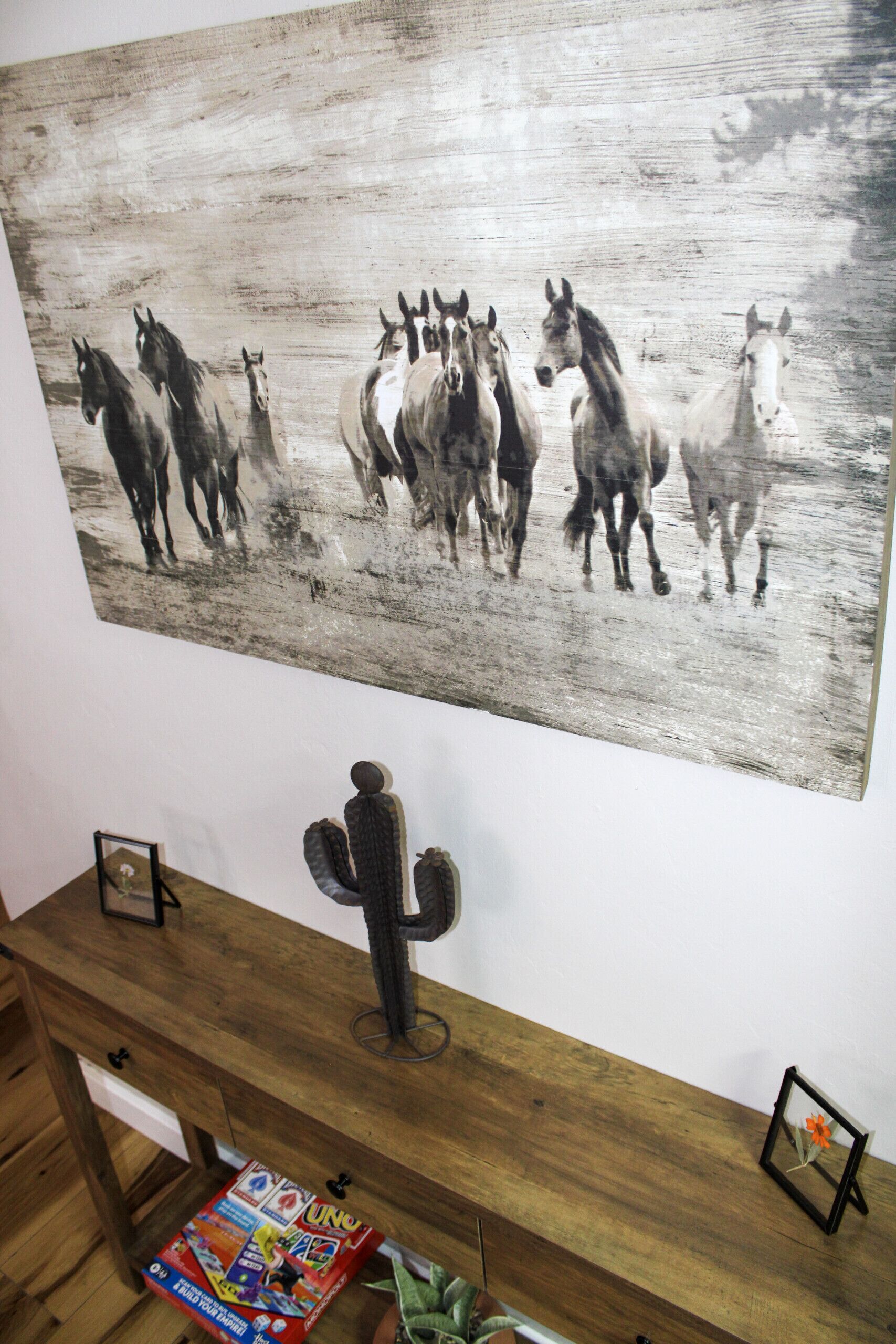 Een muur met een schilderij van paarden, een cactussculptuur en een houten bureau met een speldoos.