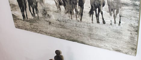A wall with a painting of horses, a cactus sculpture, and a wooden desk with a game box.