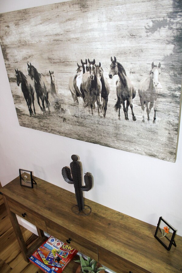 A wall with a painting of horses, a cactus sculpture, and a wooden desk with a game box.