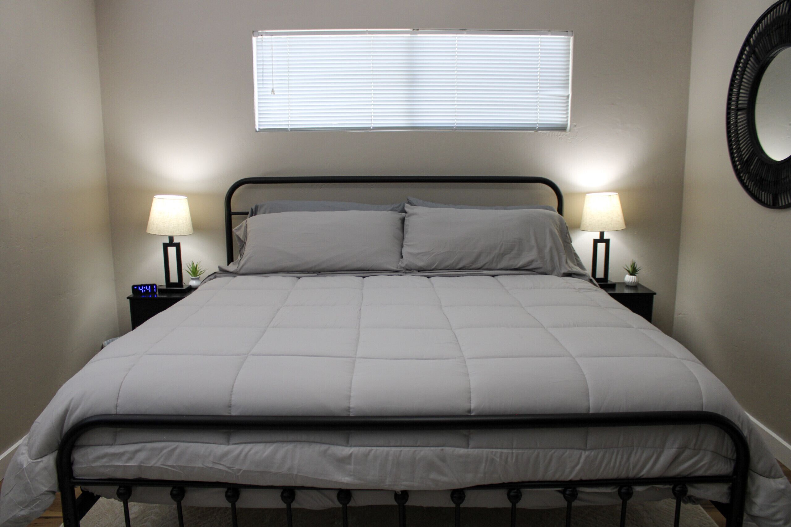 A neatly made bed with a headboard, two bedside lamps, and a wall-mounted mirror.