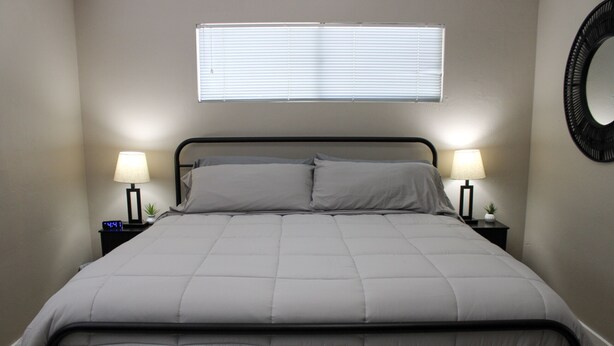 A neatly made bed with a headboard, two bedside lamps, and a wall-mounted mirror. - Serendipity Cottage (Prescott)