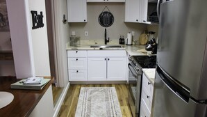 A kitchen with white cabinets, a stainless steel refrigerator, and a black wall clock. - Serendipity Cottage (Prescott)