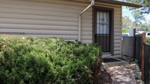 A residential building with a beige exterior, a black door with a window, and a small front yard with dense green shrubbery. - Serendipity Cottage (Prescott)
