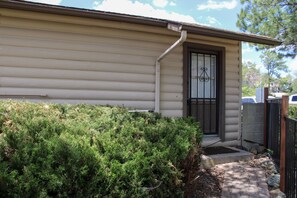 A residential building with a beige exterior, a black door with a window, and a small front yard with dense green shrubbery. - Serendipity Cottage (Prescott)