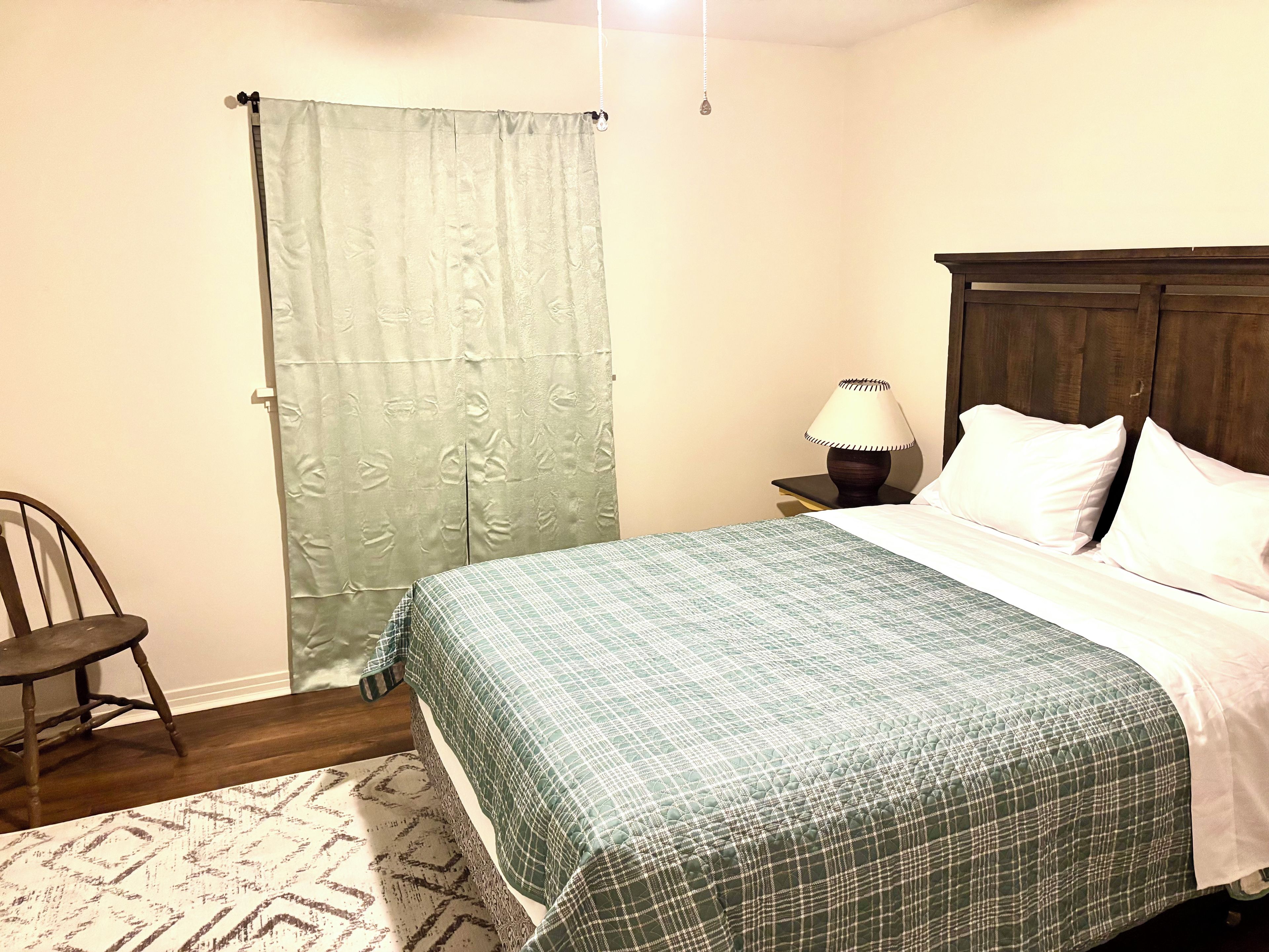 A bedroom with a bed, a nightstand, a lamp, a chair, and a patterned rug.