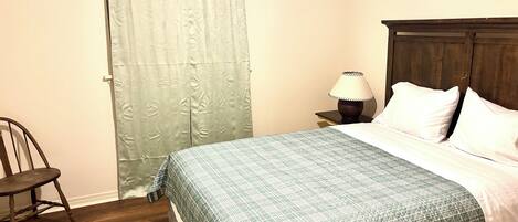 A bedroom with a bed, a nightstand, a lamp, a chair, and a patterned rug.