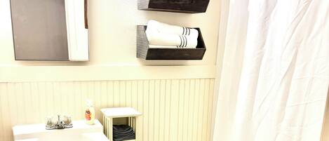 A bathroom with a white sink, toilet, and shower curtain. There are towels and a shelf above the toilet.