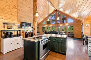 A spacious kitchen with a large island, wooden cabinets, and a stone accent wall. - 5-Bedroom Family Cabin with 3 King Beds & Mountain Views in Duck Creek Village (Duck Creek Village)