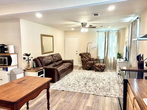 A living room with a brown leather sofa, a patterned armchair, a wooden coffee table, a patterned rug, and a ceiling fan.