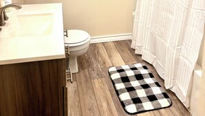 Un baño con un lavamanos blanco, inodoro y un tapete de cuadros en el suelo.