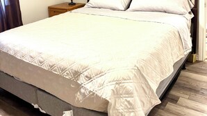 Una cama bien hecha con edredón blanco, una mesita de noche con lámpara y un espejo decorativo en la pared.