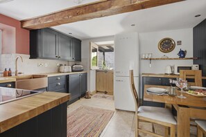 A modern kitchen with dark cabinets, a wooden dining table, and a clock on the wall. - The Tractor Shed: A Quiet Retreat Near Symonds Yat (Ross-on-Wye)