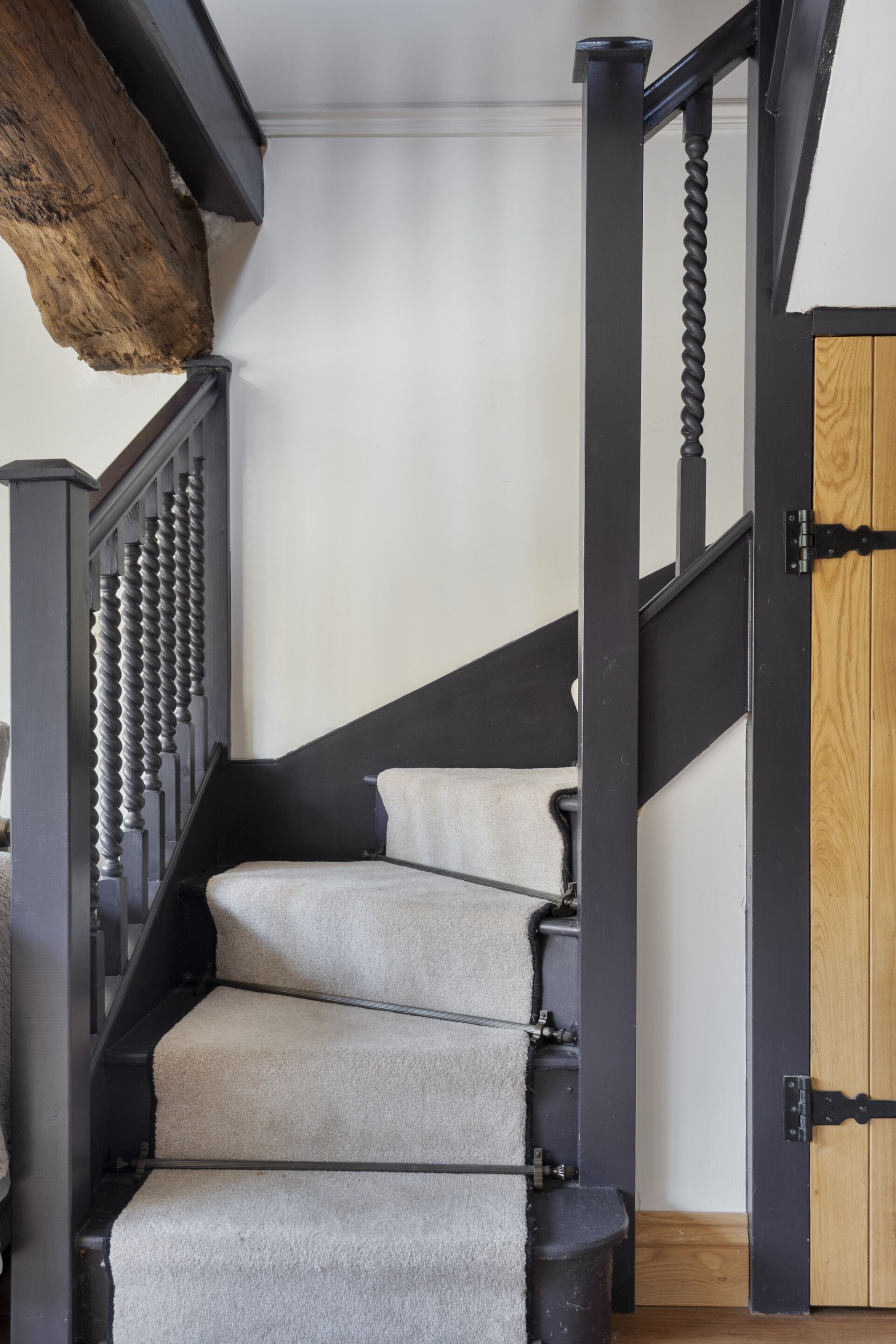 A staircase with a wooden handrail and a black balustrade, leading to a room with a wooden door.