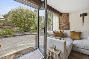 A modern living room with a glass door leading to a garden, a stone wall, and a cozy sofa with cushions. - The Tractor Shed: A Quiet Retreat Near Symonds Yat (Ross-on-Wye)